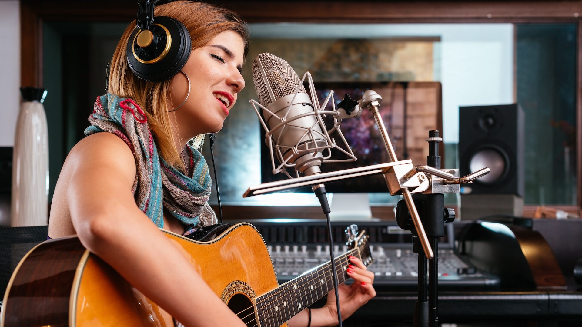 Młoda kobieta z gitarą nagrywa piosenkę w studio.