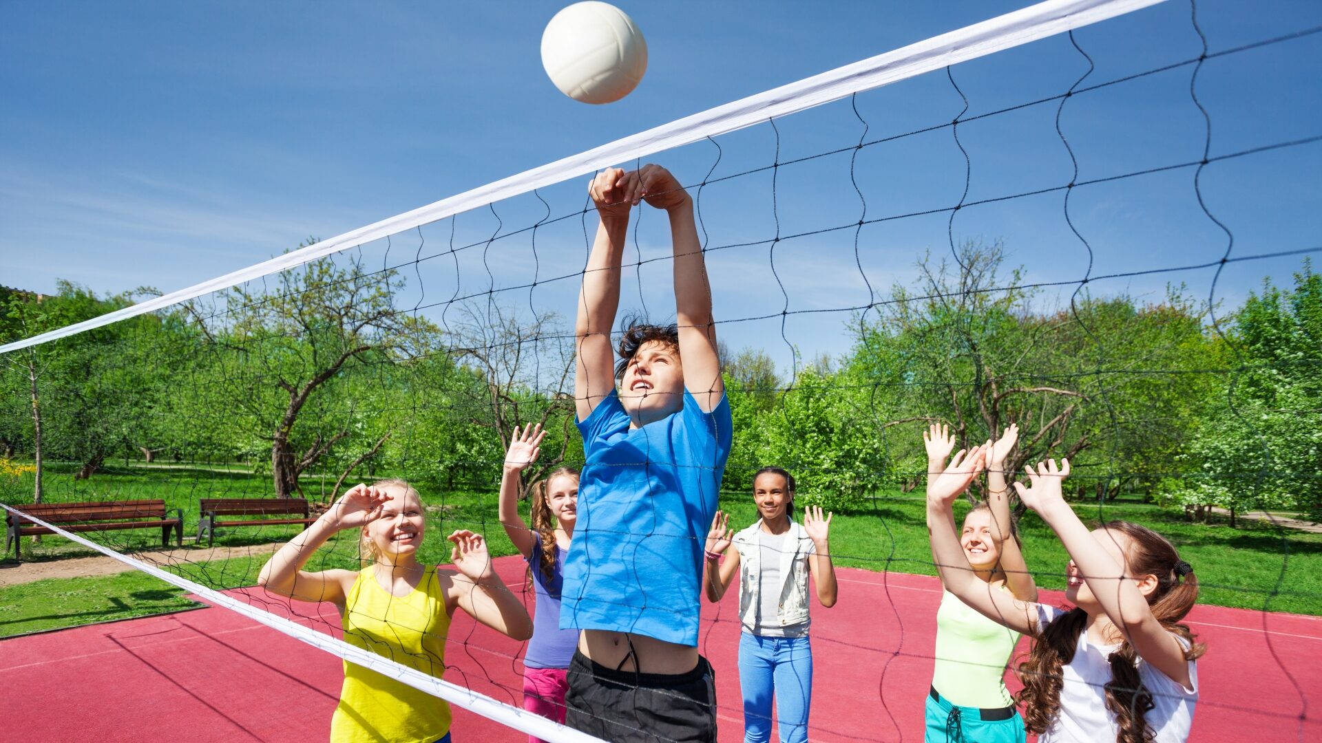 Nastolatkowie z podniesionymi rękami grają w siatkówkę